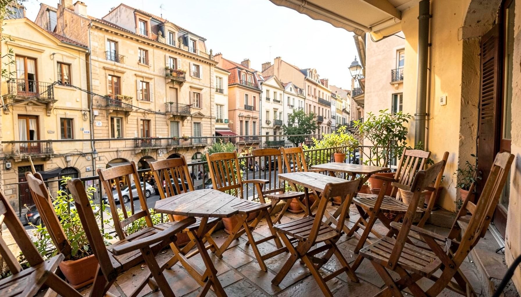 A relaxed outdoor patio with wooden chairs and small tables, overlooking a charming historic district street scene in warm afternoon light