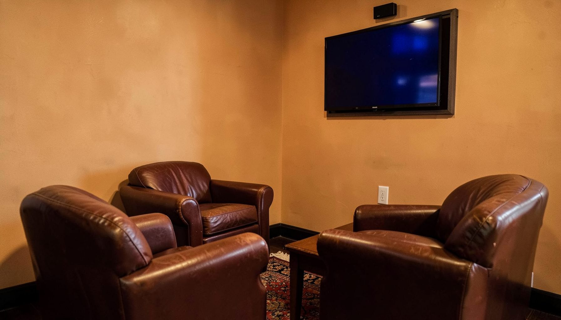 A cozy indoor lounge corner with leather armchairs and a flat-screen TV mounted on a warm-toned wall